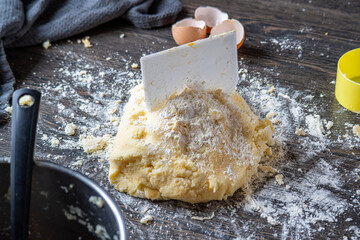 Gnocchi preparation steps: Homemade gluten free mashed potato puree dough with scraper on a dark table. Flour and eggshells in the background. Part of creating pasta dough for an Italian dish