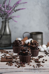 Several muffins or cupcakes with chocolate shaped cream at white table. Festive candle burns on a chocolate cake. There are chocolate chips scattered nearby