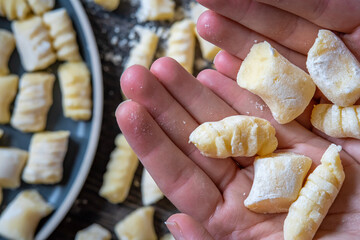 Gnocchi preparation steps: Woman's Hand showing raw uncooked homemade gluten free potato gnocchi. More gnocchi with sprinkled flour in background. Creating authentic pasta dough for an Italian dish.
