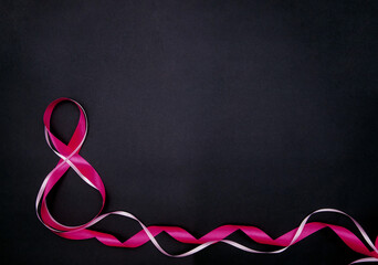 On a black background, a pink satin ribbon in the form of the number eight. Gift wrap.