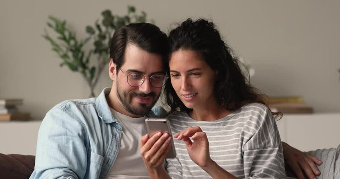 Couple sit on sofa holding smartphone celebrate online betting victory. Happy excited spouses receive special commercial offer, fantastic news, great opportunity, candid emotions moment of win concept