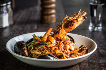 Linguine spaghetti marinara seafood dish with prawn, mussels, parsley, tomato on a white dish and wooden table
