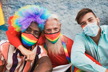 Multiracial gay men at lgbt pride event taking a selfie together while wearing protective face mask for coronavirus - Young and senior men