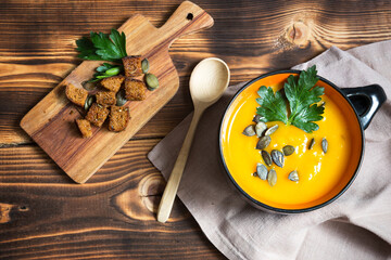 Pumpkin soup in a bowl with seeds and parsley on a wooden background. Crackers with spices on the board. Copy space