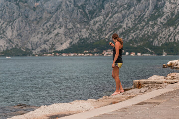A young athletic woman stands on the shore and eats an apple in the summer .Kotor bay (Boka Kotorska), Montenegro, Europe