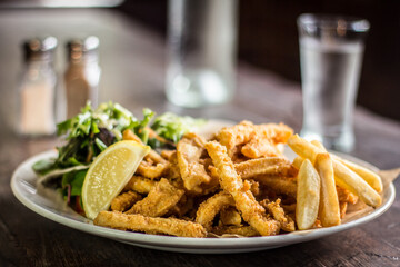 Crispy Calamari fried with cocktail sauce lemon and salad on a wooden table