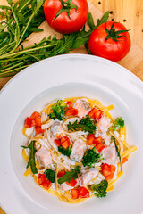 spaghetti with salmon, broccoli and tomatoes in a creamy sauce on a decorated table