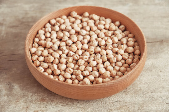 Raw chickpeas in a wooden plate on a wooden background. Top view. Copy, empty space for text