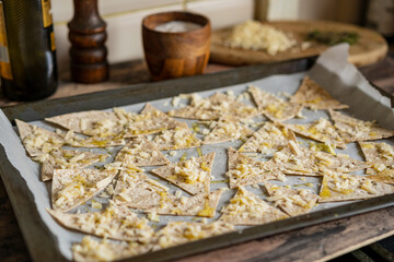 Process of cooking cheese Tortilla chips with olive oil on baking sheet before oven, homemade salty savory pastry snack in the kitchen. Selective focus with copy space.
