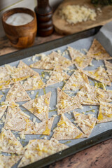 Process of cooking cheese Tortilla chips with olive oil on baking sheet before oven, homemade salty savory pastry snack in the kitchen. Selective focus with copy space.