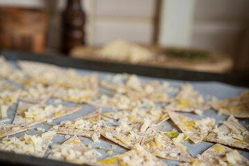Process of cooking cheese Tortilla chips with olive oil on baking sheet before oven, homemade salty savory pastry snack in the kitchen. Selective focus with copy space.