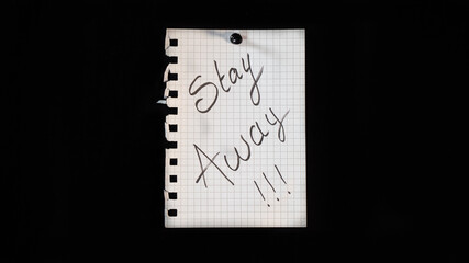 Hand written message on a ripped notebook sheet, "Stay away"