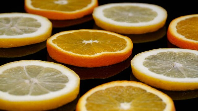 Citrus slices rotating on a black background. Slices of organic orange and lemon in 4K.  Yellow orange abstract view