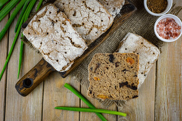 Homemade Finnish sandwich bread with prunes and dried apricots on a wooden table. Homemade bread with dried fruits and green onions on a dark background
