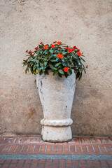 Stone flowerbed with flowering plants on the background of a stone wall on an old Italian street. Sirmione. Lombardy, Italy