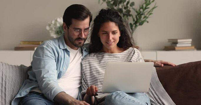 Excited overjoyed young 30s couple celebrate online bet victory, gambling game winner concept. Wife and husband sit on couch with laptop surfing internet, clients find good low price offer feels happy