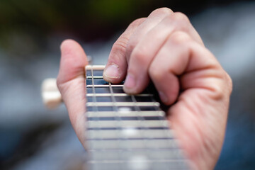 closeup of young man playing ukulele at the river in sunny field and water cordoba argentina