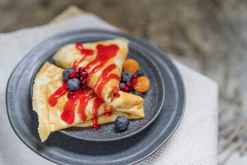 French crepes with fresh berries and fruit sauce on a plate served on wooden cutting board. Closeup view on pancakes. Tasty sweet breakfast, lunch or dessert. Selective focus, copy space.