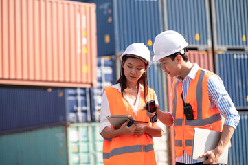 Asian dock control man and woman logistics worker wear safety helmets and protect suite working in shipping container, commercial transport background.