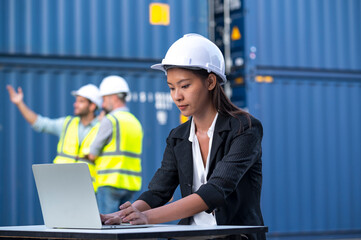 Woman logistics worker  wear safety helmets and protect suite working and checking product with laplets in shipping container, commercial transport background.