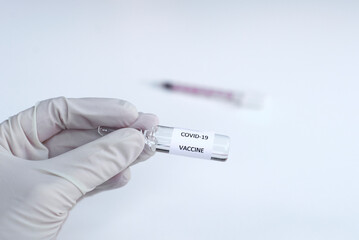 Obraz premium Medical worker hand in medical white glove holding a glass vaccine for vaccination against the COVID-19, SARS-CoV-2 coronavirus pandemic on white background with syringe