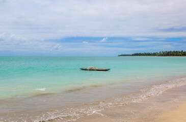 Praia com água cristalina, nuvens no céu e barquinho