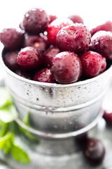 Deep red cherries freshly washed with drops of water in a metal bowl with mint leaves and drops of water, photography of very bright and refreshing food