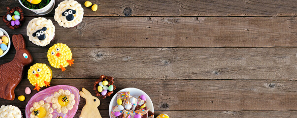 Easter table scene with an assortment of desserts and sweets. Overhead corner border on a wood banner background. Spring holiday food concept. Copy space.