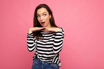 Photo of young positive happy surprised astonished beautiful brunette woman with sincere emotions wearing casual striped pullover isolated on pink background with copy space. Wow concept