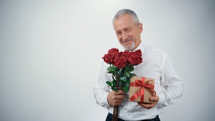 A funny old man with a beard, with a gift box and red roses in his hands wants