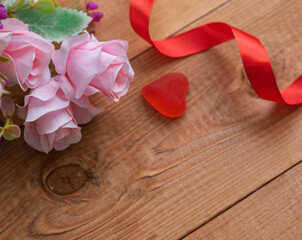 Pink roses on a dark wooden background with a red ribbon and a heart. Concept of Valentine's day. Copy space for text.