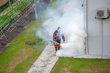 Healthcare worker using Fogging machine spraying chemical to eliminate mosquitoes and kill larvae to fight against the spread of dengue fever, Zika virus or Malaria at a residential area.