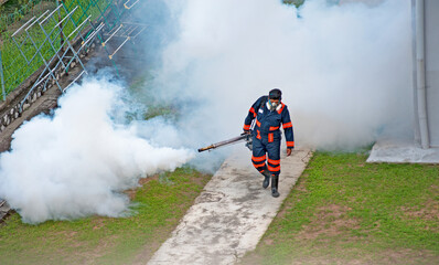 Healthcare worker using Fogging machine spraying chemical to eliminate mosquitoes and kill larvae to fight against the spread of dengue fever, Zika virus or Malaria at a residential area.
