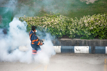Healthcare worker using Fogging machine spraying chemical to eliminate mosquitoes and kill larvae to fight against the spread of dengue fever, Zika virus or Malaria at a residential area.
