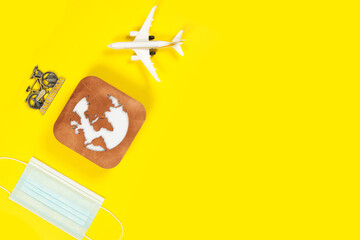 Plane model, face mask and earth model on a yellow background. Flight impact of coronavirus (COVID-19) concept.