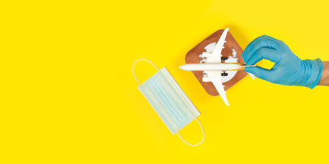 Plane model in hand, face mask  and earth model on a yellow background. Hands in gloves. Flight impact of coronavirus (COVID-19) concept. Africa.