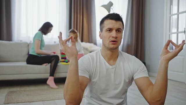 Nervous domestic atmosphere. Close up of father meditating at home while his family playing in living room