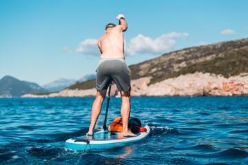 Young athletic man paddling on a SUP stand up paddle board in blue water sea in Montenegro