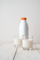 Two filled glasses of milk and a bottle on a white background. Side view, vertical orientation. The concept of food products.