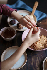 Child hands making sweet balls cookies called Potato of marzipan, biscuits, cocoa. Process of dessert cooking, wooden table with ingredients. Selective focus, copy space