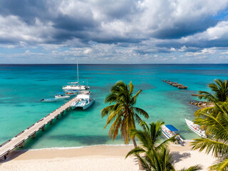 Obraz premium Aerial drone view of the paradise beach with old and new pier, boats, yacht, palm trees and blue water of Caribbean Sea, Saona island, Dominican Republic