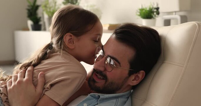 Little daughter whispers in ear confides a secret to daddy, close up. Loving dad talk to small child, family enjoy communication sit at home on chair. Harmonic friendly relation, understanding concept