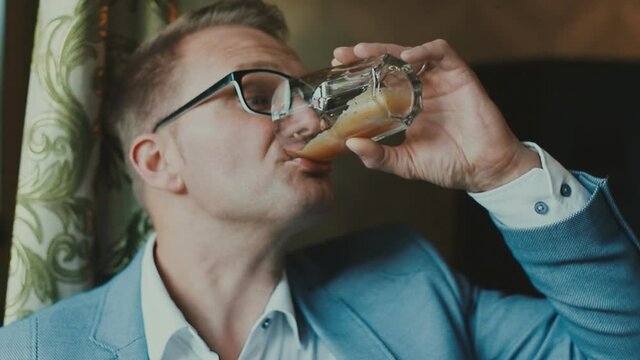 A young guy in a suit is funny and emotionally drinking a carbonated drink from a glass and licks his lips deliciously. Businessman fooling around on camera.