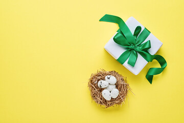 Quail eggs in nest and gift box with green ribbon on yellow trend color background. Easter minimal creative horizontal composition with copy space. Spring Happy Easter holiday card. Top view.