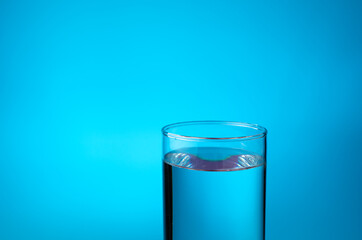 A transparent glass filled with water on a blue background. Side view with copy space. The concept of water resources.