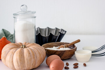 Ingredients for baking with pumpkin on a white table in the kitchen, flour, sugar, pumpkin, eggs, nuts, baking accessories, muffin molds. Home baker concept,authentic home hobby, cooking at home