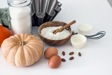 Fototapeta na wymiar Ingredients for baking with pumpkin on a white table in the kitchen, flour, sugar, pumpkin, eggs, nuts, baking accessories, muffin molds. Home baker concept,authentic home hobby, cooking at home