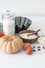 Ingredients for baking with pumpkin on a white table in the kitchen, flour, sugar, pumpkin, eggs, nuts, baking accessories, muffin molds. Home baker concept,authentic home hobby, cooking at home