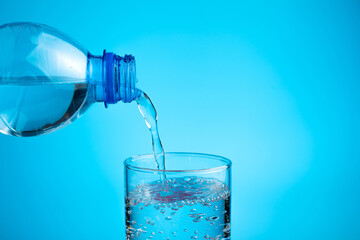 The process of pouring water into a glass on a blue background. Side view, horizontal orientation. The concept of water resources.