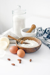Obraz na płótnie Canvas Homemade baking ingredients and accessories. A jar of sugar, a cup of flour, eggs, a whisk, a cake pan, a napkin, nuts on a white table. Home hobbies authentic cooking concept, close-up, copy space